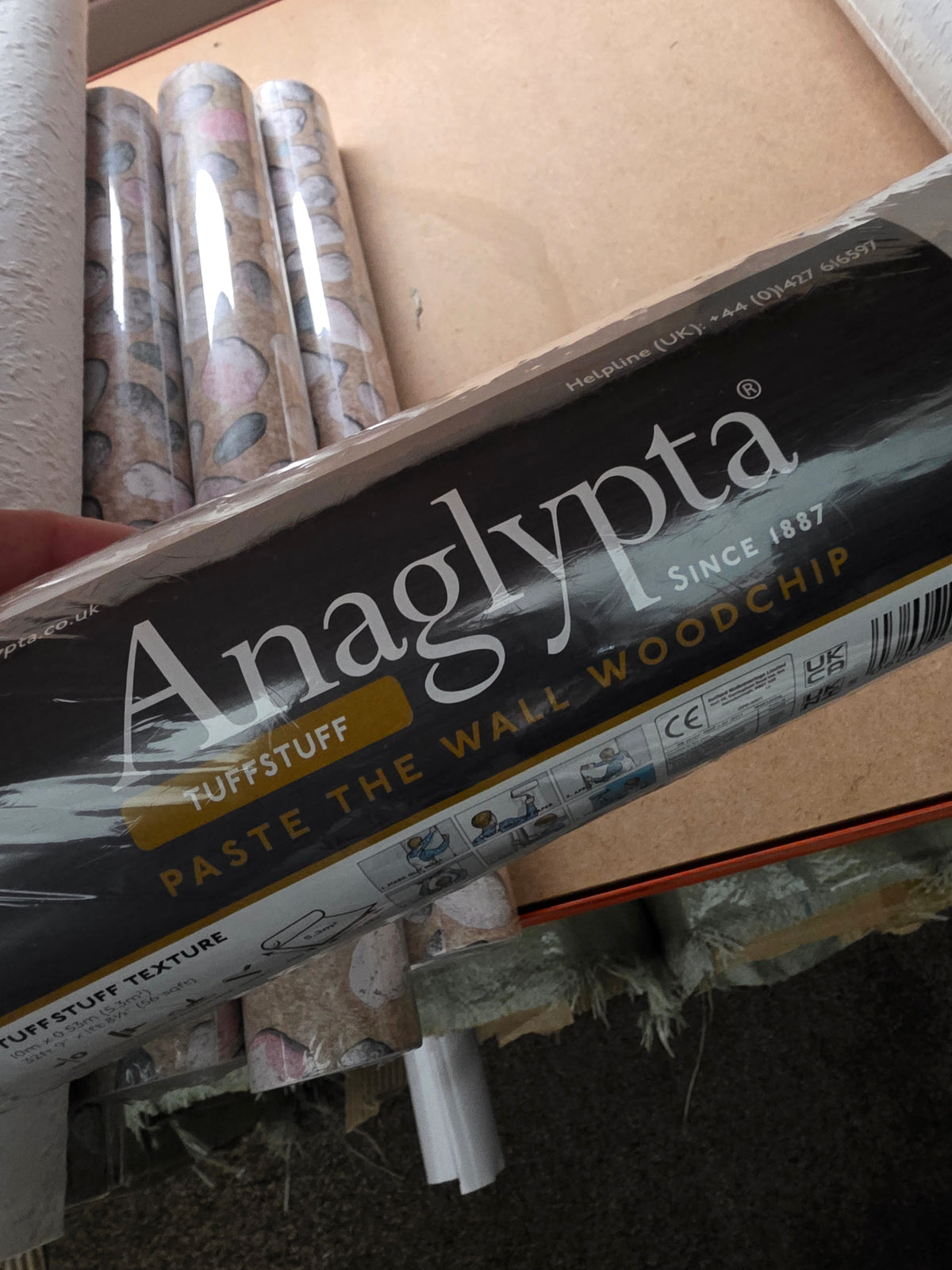 Wood chip wallpaper from Budget Interiors, showing three rolls with textured, natural wood grain design for interior walls.