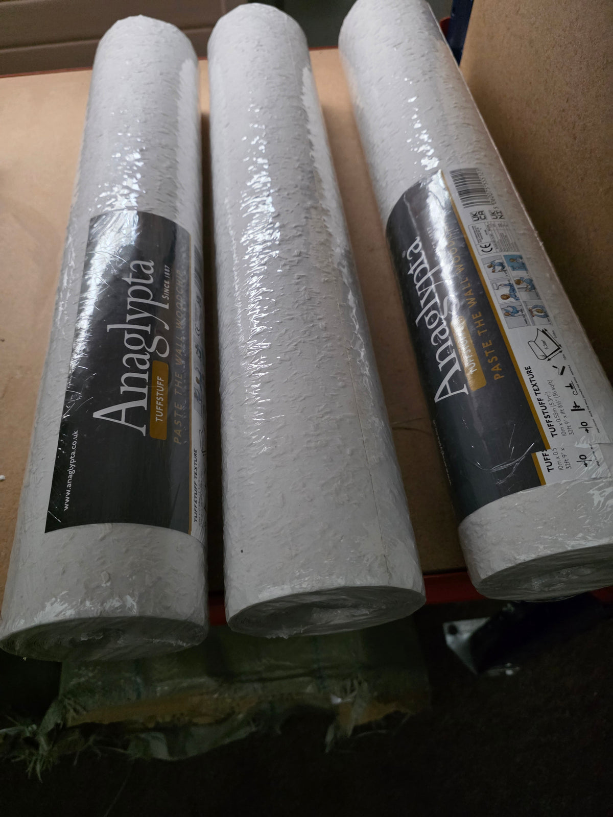 Wood chip wallpaper from Budget Interiors, showing three rolls with textured wood grain pattern for wall decorating.